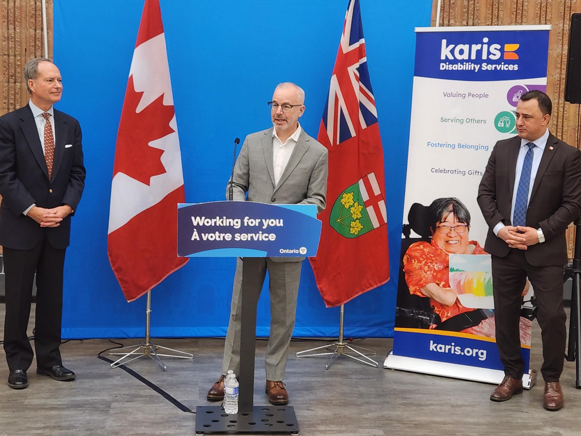 Image of three leaders speaking at a funding announcement with the Canadian flag and Ontario flag in the background. A podium states 'working for you' in English and French as Ontario's slogan.