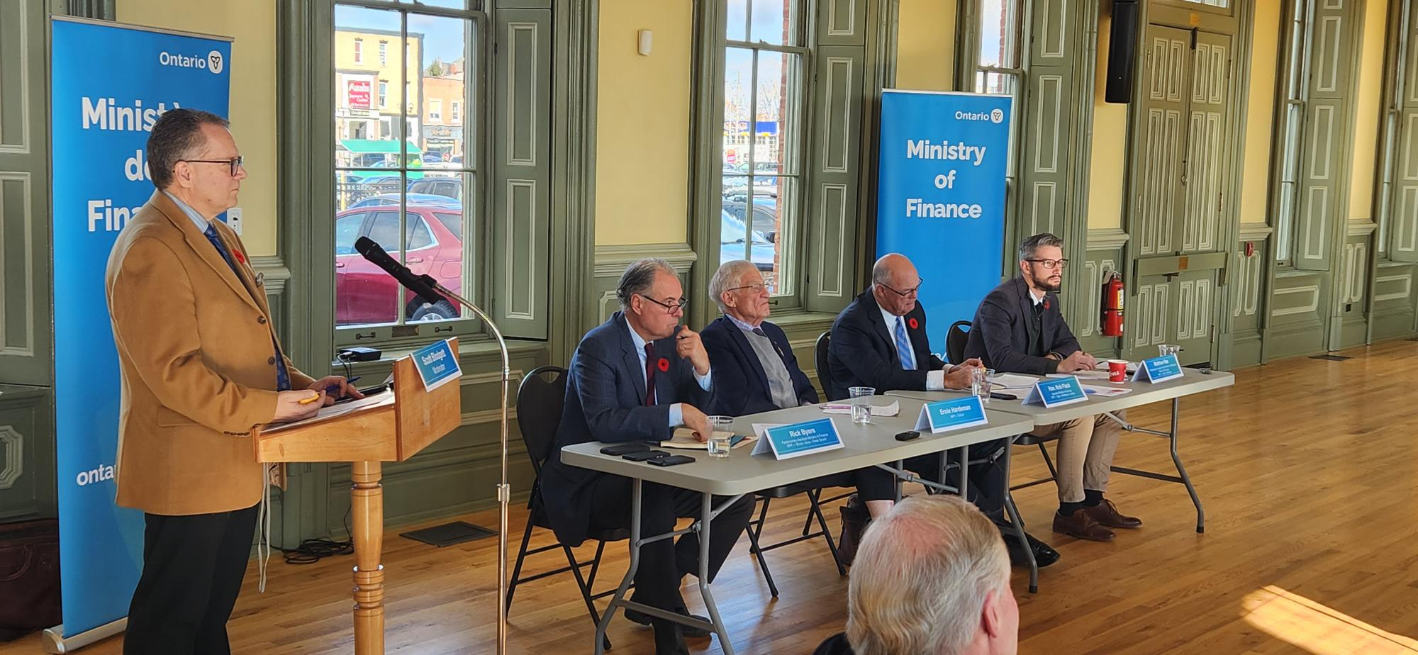 Image of 4 men sitting at a table listening to a speech at the Ministry of Finance. 